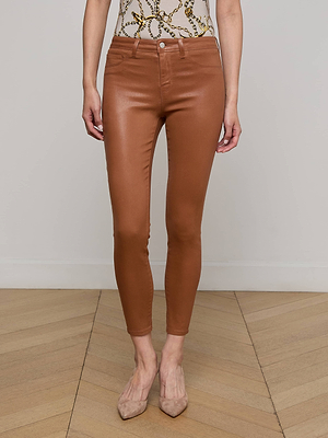 A person indoors wears the Margot Coated Cropped Skinny Jean in caramel brown with beige pointed-toe heels and a patterned sleeveless top, standing against a light-colored wall and wooden floor.