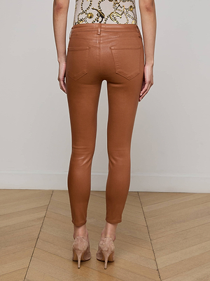 A woman stands indoors on a wooden floor, shown from the back, wearing Margot Coated Cropped Skinny Jean, a patterned top, and beige high-heeled shoes.