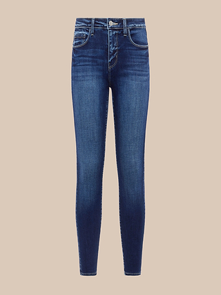 Jean skinny court Margot : jean skinny bleu à taille haute en denim stretch haut de gamme, doté dune fermeture à bouton et à fermeture éclair ainsi que de poches avant et arrière, présenté sur un fond beige.
