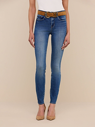 Model showcases the Marguerite Skinny Jean, a high-rise blue skinny fit made from stretch denim, paired with a brown belt and tan pointed-toe heels. Only the body from shoulders down is visible against a beige background.