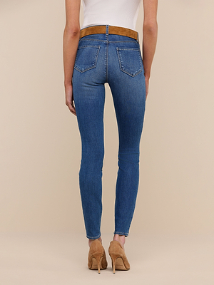 A person is shown from the back, standing against a neutral background, wearing Marguerite Skinny Jean in high-rise blue stretch denim with a brown belt, a white top, and beige high-heeled shoes.