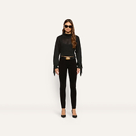A model wears high-rise black Marguerite Corduroy Skinny Pant with a black fringe-sleeved sweater, a black belt with a gold buckle, and black pumps.