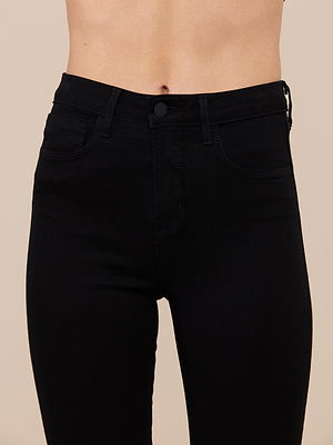 A close-up of a person wearing the Marguerite Skinny Jean in high-waisted black high-recovery fabric, highlighting the waistband, pockets, and button against a neutral beige background. The persons torso is shown without revealing their face.