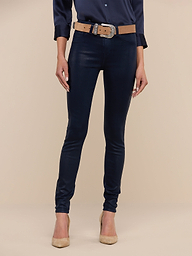 A person stands against a plain background, wearing a navy blouse, the Marguerite Coated Skinny Jean in navy with a tan belt, and tan high-heeled shoes. The photo is cropped at the shoulders.