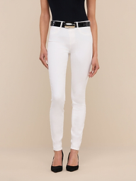 A woman stands against a plain background, wearing a black sleeveless top, the Marguerite Skinny Jean in white with a black belt, and black pointed-toe shoes. Only her body from the shoulders down is visible.