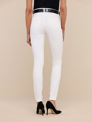 A person is shown from the back against a beige background, wearing Marguerite Skinny Jeans in white, paired with a black belt and black high-heeled shoes.