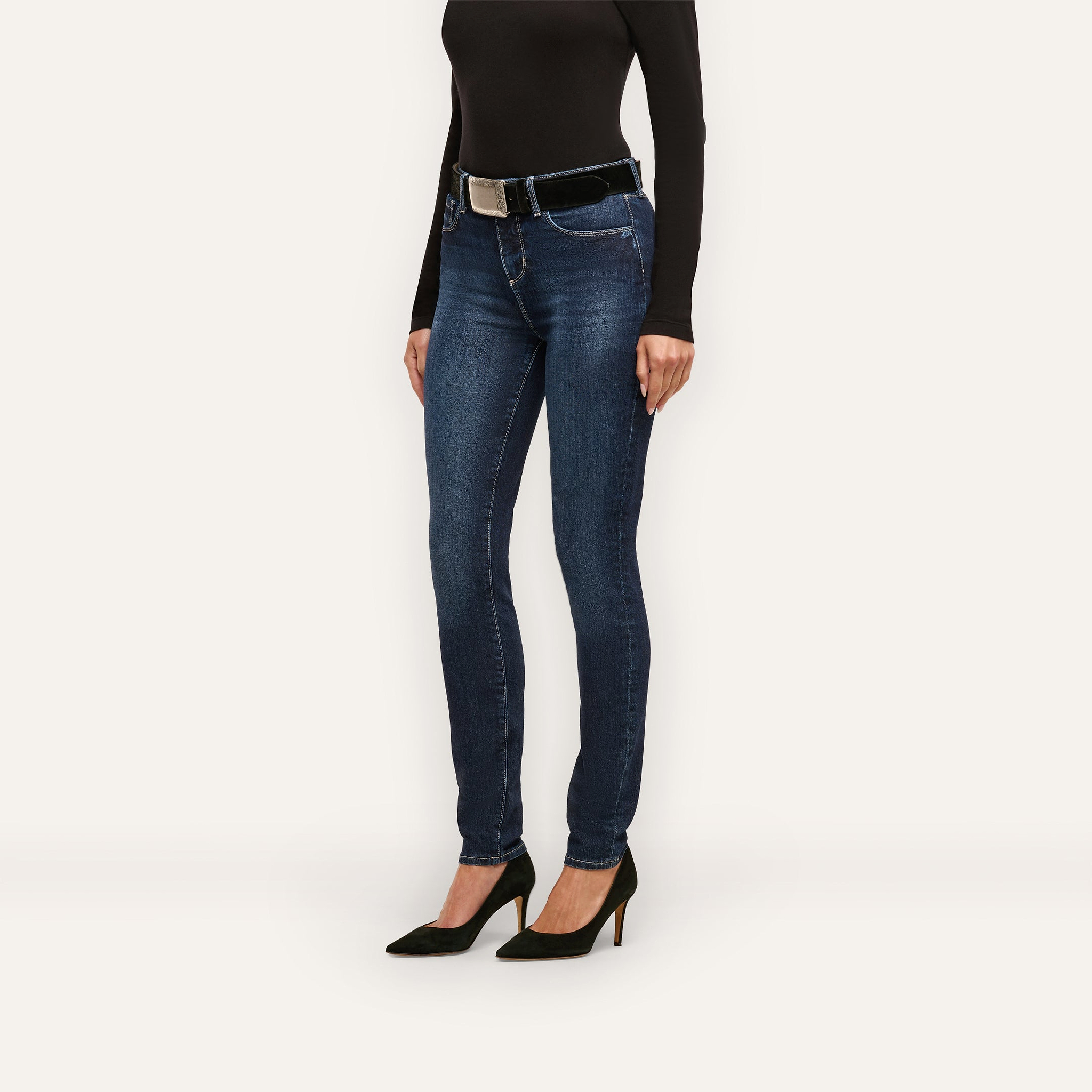 A person wearing Marguerite Skinny Jean high-rise, stretch denim skinny jeans, a black long-sleeved shirt, a black belt, and black high-heeled pumps.