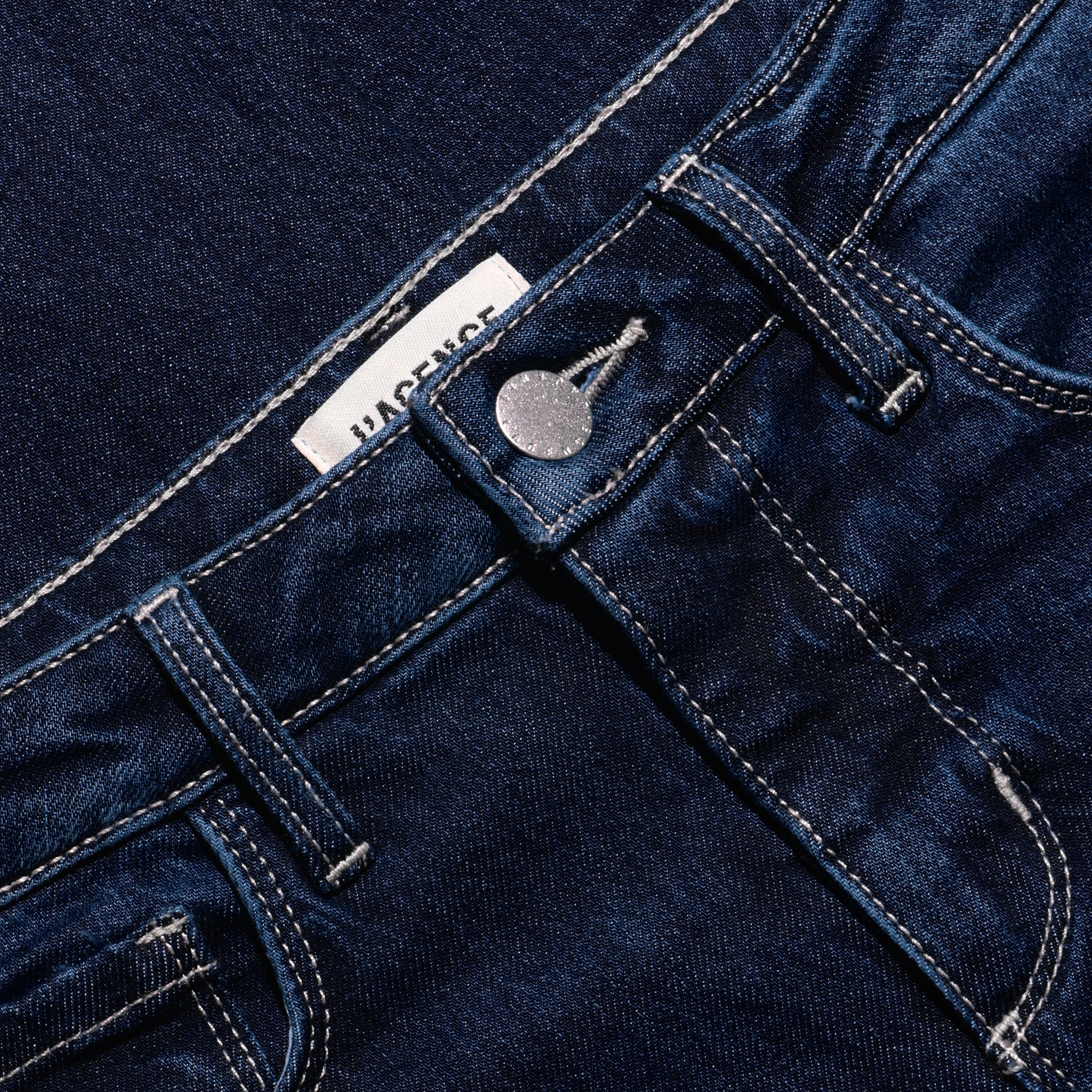 Close-up of Marguerite Skinny Jean high-rise dark blue stretch denim, showing the waistband, silver metal button, and contrast stitching.