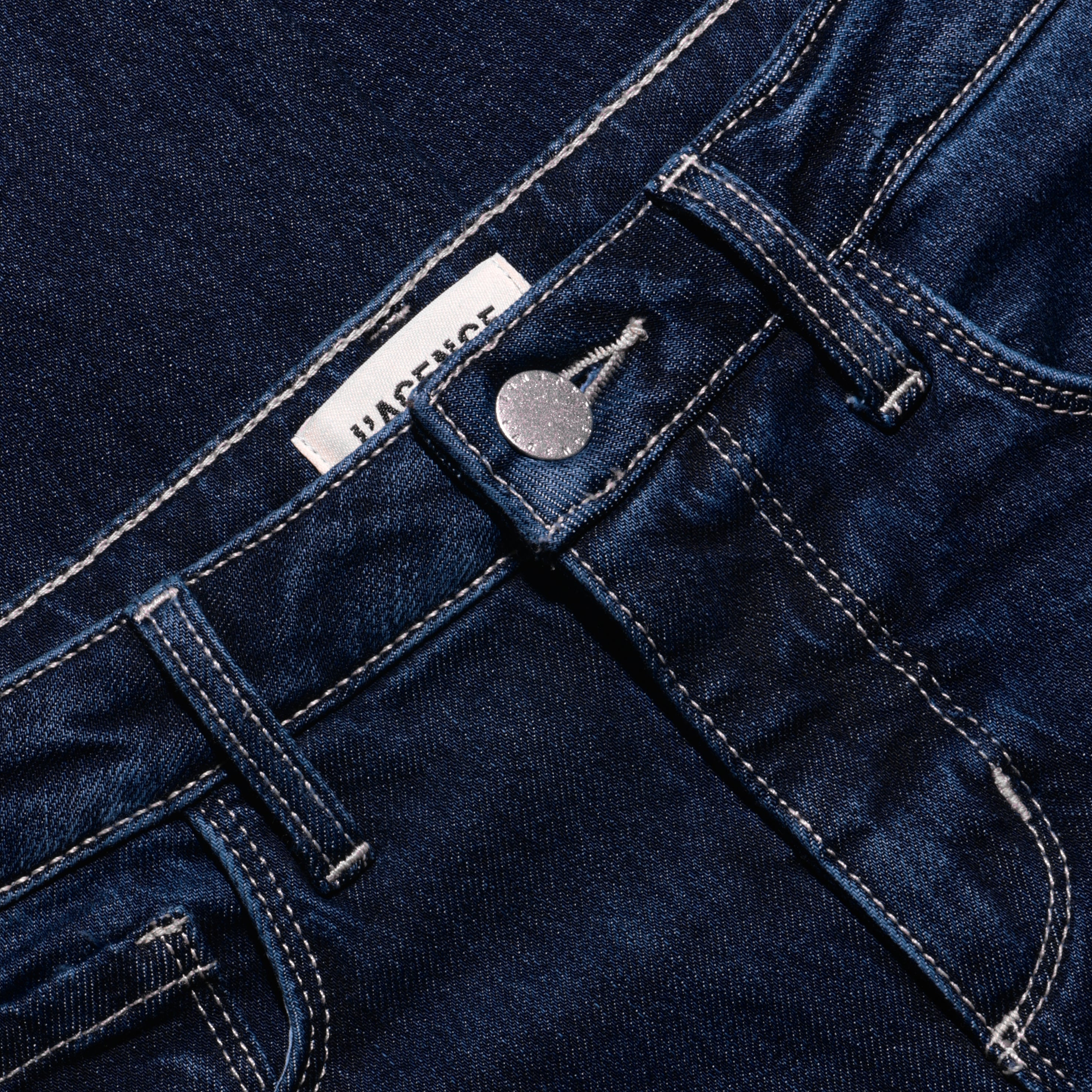 Close-up of Marguerite Skinny Jean high-rise dark blue stretch denim, showing the waistband, silver metal button, and contrast stitching.