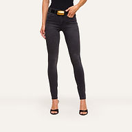 Wearing Marguerite Skinny Jean in black high-recovery fabric, a black top, high-heeled sandals, and a black belt with a large gold buckle, this person stands against a plain light background.