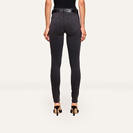 A woman faces away, wearing the Marguerite Skinny Jean in black with a 30-inch inseam and a black sleeveless top, paired with high heels, against a plain light background.