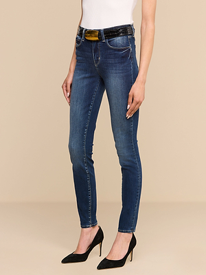 Vêtue dun haut blanc sans manches, dun jean skinny Marguerite en denim stretch haut de gamme, dune ceinture noire texturée et descarpins noirs, une personne se tient debout devant un fond beige.