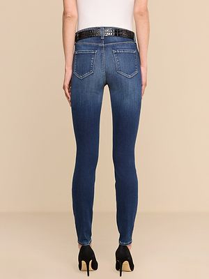 On voit une personne de dos sur un fond beige, vêtue dun haut blanc, dun jean skinny « Marguerite » à poches arrière en denim stretch haut de gamme, dune ceinture noire texturée et de chaussures à talons hauts noires.