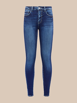 Le jean skinny Marguerite est un jean skinny bleu à taille haute, confectionné dans un denim stretch haut de gamme, avec un délavage délavé, cinq poches et une fermeture à bouton et fermeture éclair, présenté sur un fond beige uni.