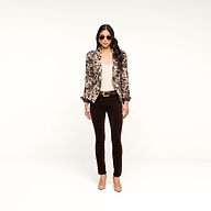 A woman stands against a white background, facing forward with her hands by her sides. She wears sunglasses, a patterned blazer over a light top, the Marguerite Velvet Skinny Jean with a belt, and beige heels.