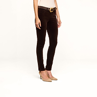A person wearing the Marguerite Velvet Skinny Jean in dark brown, a beige top, a black belt with a gold buckle, and beige high heels stands against a plain white background.
