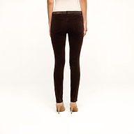 A person stands facing away, wearing the Marguerite Velvet Skinny Jean in high rise dark brown stretch velvet and beige high heels, with their arms relaxed by their sides against a plain white background.