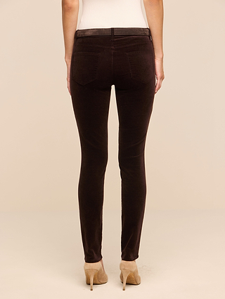 Person wearing Marguerite Velvet Skinny Jean in dark brown—a high-rise skinny pant crafted from stretch velvet—and beige high-heeled shoes, standing with their back facing the camera against a plain, light background.