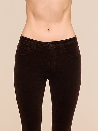 Someone is modeling the Marguerite Velvet Skinny Jean, shown from waist to mid-thigh against a beige background. The image highlights the person’s torso and hips, while their face and lower legs remain out of view.