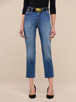 A woman models the Sada Slim-Leg Cropped Jean in premium stretch denim with a black belt and heels; her upper body is out of frame, set against a plain beige background.