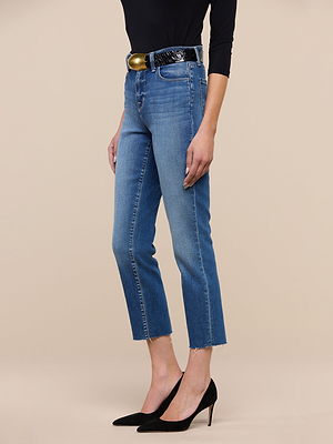 Wearing Sada Slim-Leg Cropped Jean, a black long-sleeve top, wide black belt with a gold buckle, and black high heels, a person stands against a beige background.