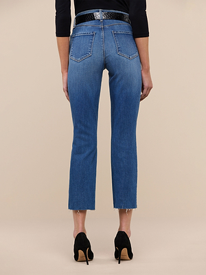 A person stands facing away, wearing Sada Slim-Leg Cropped Jean with raw hems, a black belt, and black heeled shoes against a plain beige background.