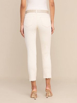 Vor einem schlichten beigen Hintergrund steht eine Person mit dem Rücken zur Kamera und trägt eine „Sada Slim-Leg Cropped Jean“ mit ausgefransten Säumen, einen beigen, strukturierten Gürtel sowie beige Sandalen mit Absatz.