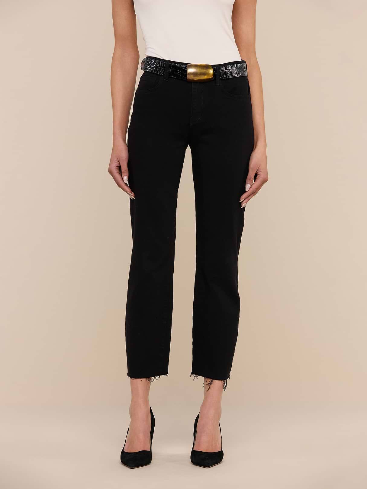 A person stands against a white background, wearing a sleeveless white top and Sada Slim-Leg Cropped Jeans with frayed hems, styled with a black belt featuring a gold buckle and black open-toe heels. Only the body below the shoulders is visible.