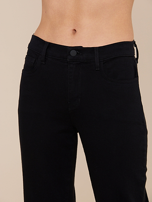 A close-up of a person wearing the Sada Slim-Leg Cropped Jean in black, shown from waist to mid-thigh against a plain beige background, with their midriff visible.