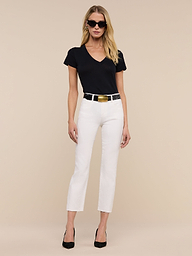 A woman stands against a plain white background, wearing sunglasses and posing with her hands by her sides. She is dressed in a black V-neck shirt, the Sada Slim-Leg Cropped Jean with stretch denim, a black belt, and black heels.