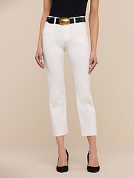 A person wearing a black top, the Sada Slim-Leg Cropped Jean in white, a black belt with a gold buckle, and black heels stands against a plain white background.