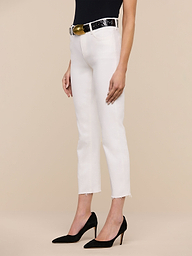 A woman stands against a white background wearing the Sada Slim-Leg Cropped Jean in stretch denim, paired with a black belt with a gold buckle, a black sleeveless top, and black high heels.