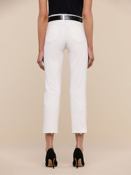 A person stands facing away, wearing the Sada Slim-Leg Cropped Jean—a high-rise white jean with frayed hems—paired with a black belt, black heels, and a dark top, against a plain white background.