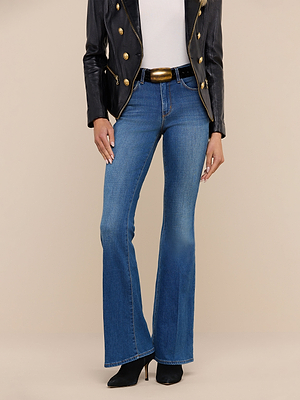 A person in a black leather jacket with gold buttons, white top, Bell Flare Jean in premium stretch blue denim, black belt with gold buckle, and black pointed-toe heeled boots stands against a plain beige background.