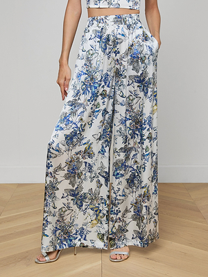 A person wearing Lillian Silk Wide-Leg Pant with a blue, yellow, and green floral butterfly print, a matching crop top, and heeled sandals stands on a light wooden floor.