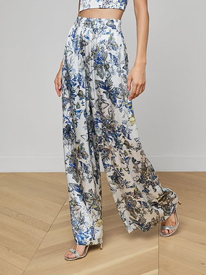 Wearing the Lillian Silk Wide-Leg Pant in a blue, yellow, and gray butterfly print with an elasticized waistband and strappy silver heels, a person stands on a light wooden floor against a plain white background.