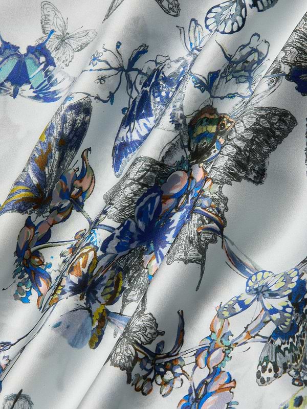 Close-up of the Lillian Silk Wide-Leg Pant in white, showcasing a blue, yellow, and black butterfly print with delicate floral patterns and softly draped folds.
