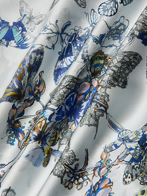 Close-up of the Lillian Silk Wide-Leg Pant in white, showcasing a blue, yellow, and black butterfly print with delicate floral patterns and softly draped folds.