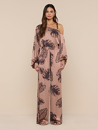 A woman models the Lillian Satin Pant, featuring an ultra-wide silhouette and a dark palm leaf print on pink satin. She stands against a plain white background, looking forward with a neutral expression.
