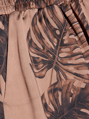 Close-up of the Lillian Satin Pant’s brown and beige palm leaf print with large overlapping monstera leaves and a gathered, elastic waistband—perfect for an ultra-wide pant.