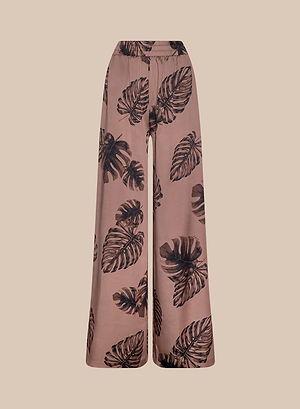 The Lillian Satin Pant features a bold black palm leaf print on light brown satin and is showcased against a plain beige background.