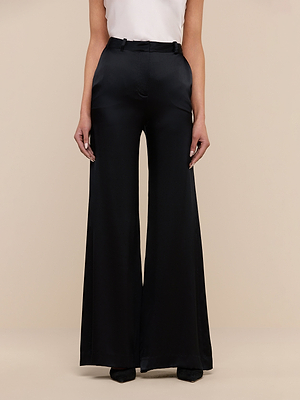 Wearing the Pilar Silk Wide-Leg Pant in black, styled with a white sleeveless top, a model stands against a neutral background, showing only the lower half of the body.