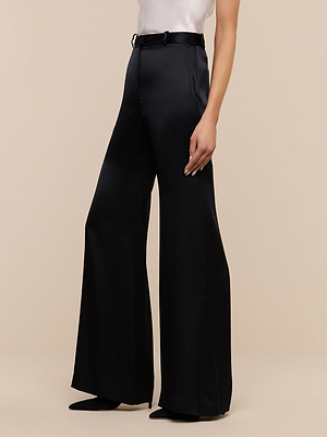 A person in high-waisted Pilar Silk Wide-Leg Pants in black and a tucked-in white sleeveless top stands against a plain beige background.