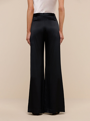 A person is shown from the back, wearing a white top and high-waisted black Pilar Silk Wide-Leg Pant with belt loops and welt pockets. The background is plain beige.