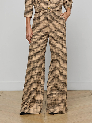 A person stands on a light wood floor wearing the Pilar Tweed Wide-Leg Pant in a beige and black check, paired with a matching cropped jacket. One hand is in their pocket and their face is not visible.