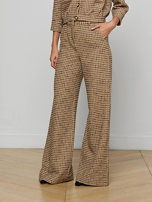 Wearing the Pilar Tweed Wide-Leg Pant and a matching long-sleeve top in Italian windowpane tweed, a person stands on a wooden floor with one hand in their pocket, showcasing a refined checkered look; their face isn't visible.
