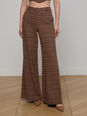 A person wears the L'AGENCE Pilar Houndstooth Wide-Leg Pant with pointed-toe heels, standing on a wooden floor against a plain light-colored wall.