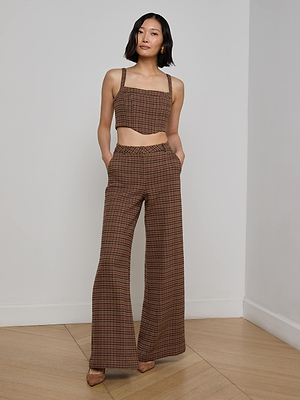 A woman with shoulder-length dark hair stands in a corner, wearing the L'AGENCE Pilar Houndstooth Wide-Leg Pant and matching crop top, one hand in her pocket and pointed-toe heels on her feet.