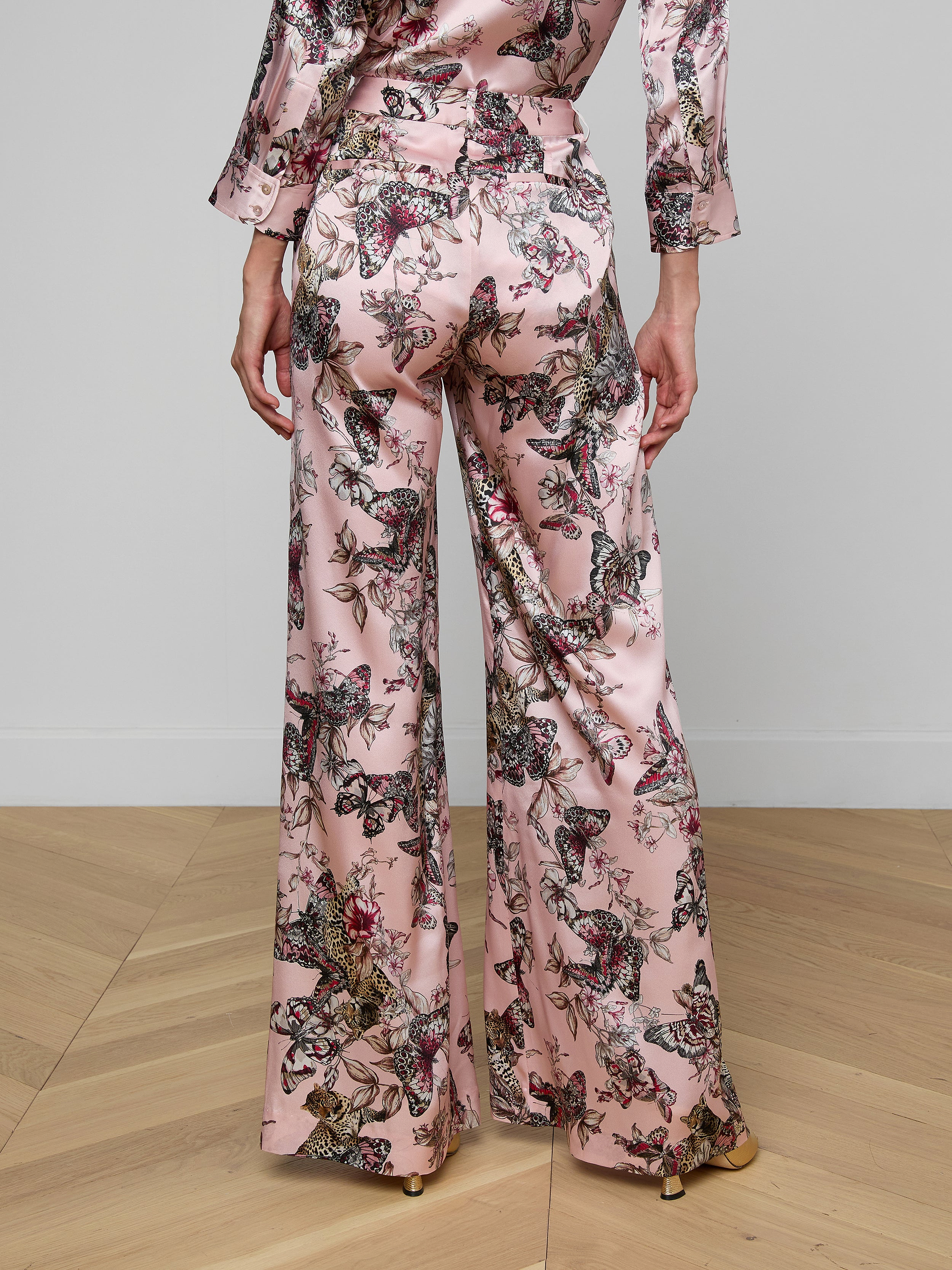 A person wearing the Pilar Silk Wide-Leg Pant in a pink, butterfly jungle print satin, shown from the back against a plain background.
