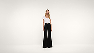 A woman stands in a white room wearing a white t-shirt tucked into high-waisted black wide-leg pants with a black belt.